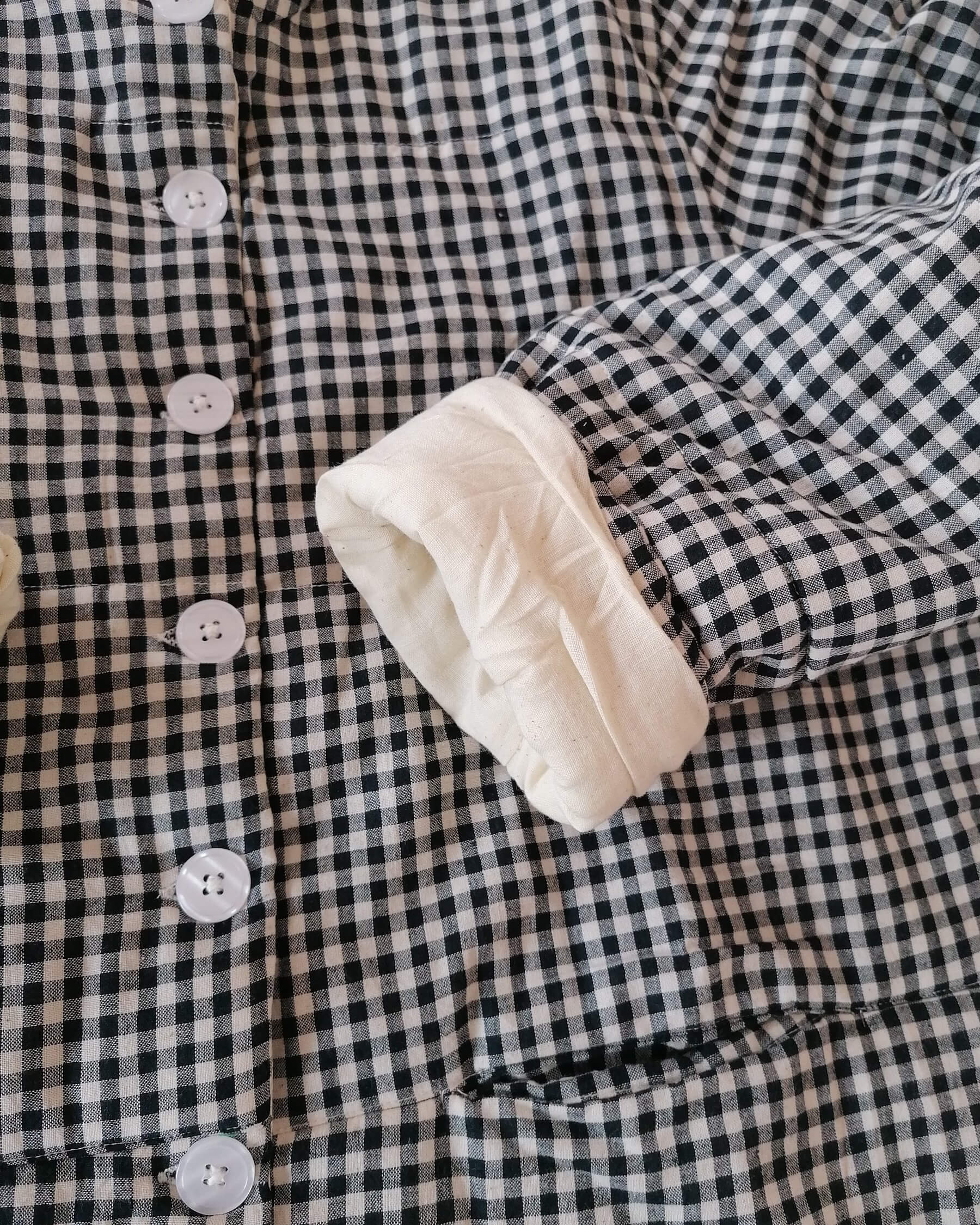 Close-up of a black and white gingham quilted jacket with a soft cream-colored lining visible on the cuff.