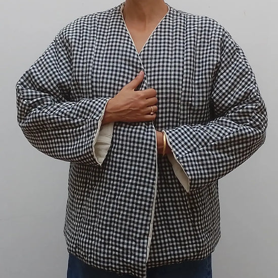 Wrap around quilted black and white gingham v neck jacket coat on model  with blue jeans on a grey background