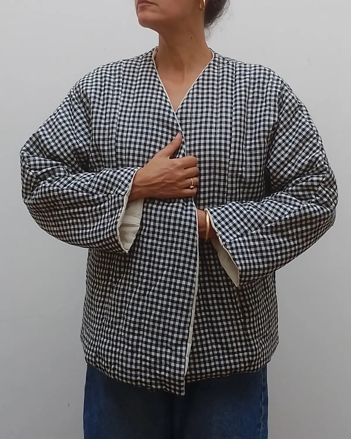 Wrap around quilted black and white gingham v neck jacket coat on model  with blue jeans on a grey background