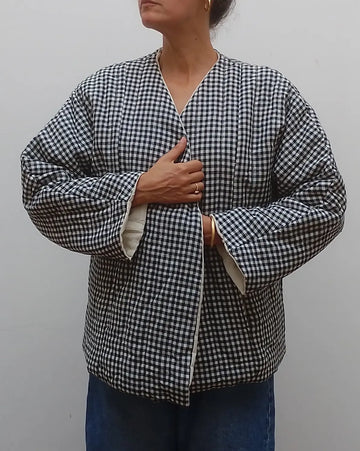 Wrap around quilted black and white gingham v neck jacket coat on model  with blue jeans on a grey background