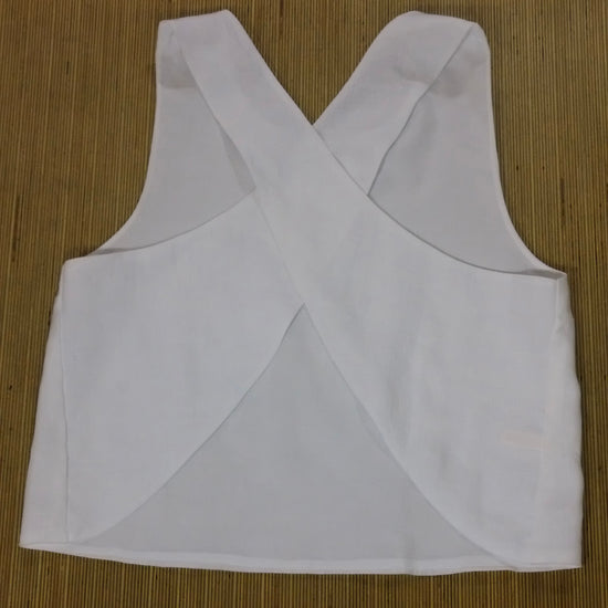 White sleeveless crop top with a crossed criss-cross back design, laid flat on a brown bamboo mat background.