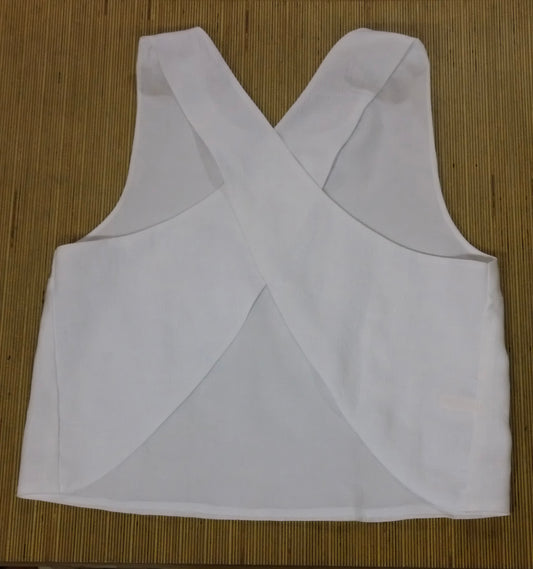 White sleeveless crop top with a crossed criss-cross back design, laid flat on a brown bamboo mat background.