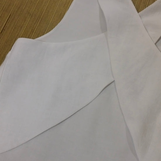 A close-up of a white sleeveless cross back top laid flat on a woven tan mat.