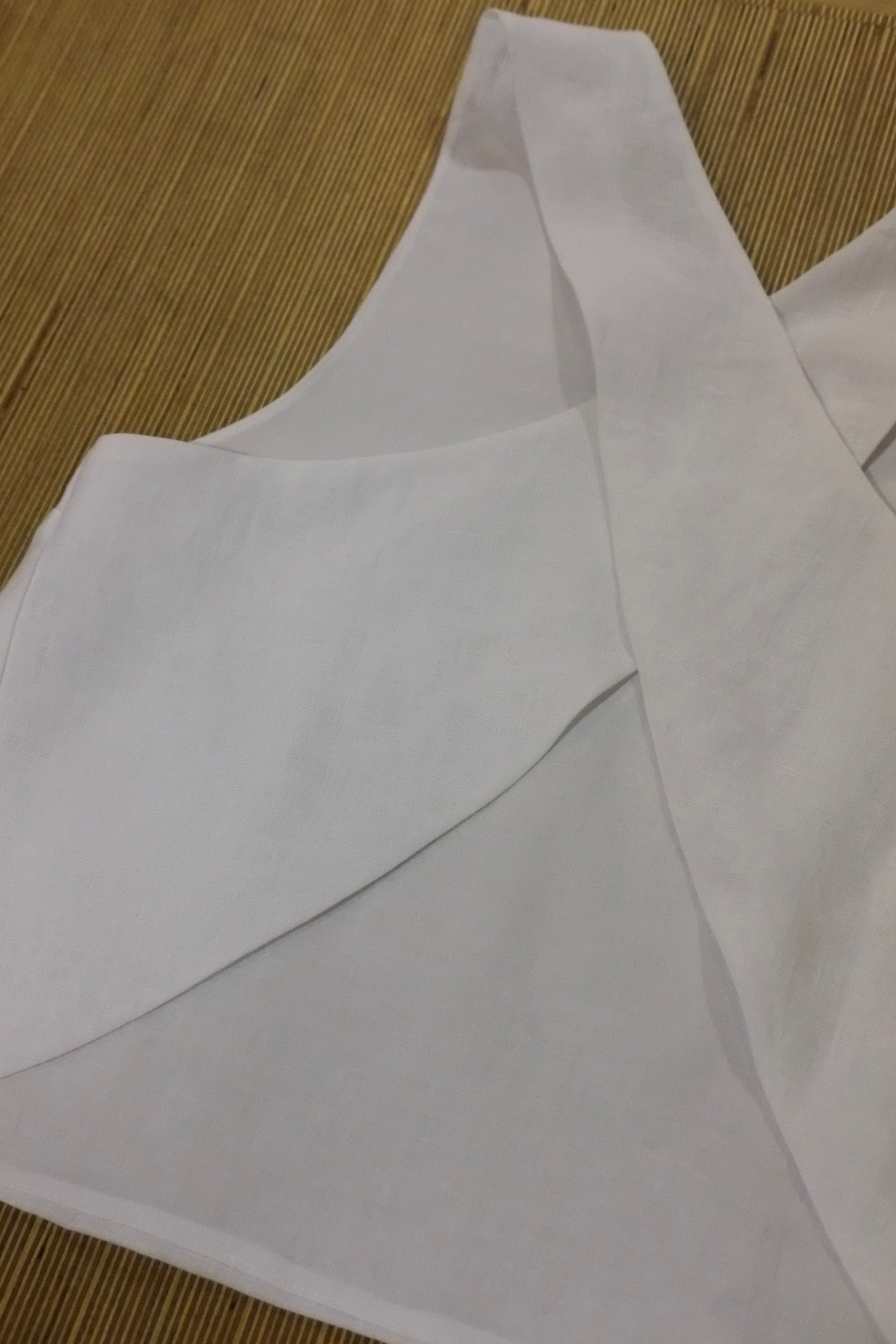 A close-up of a white sleeveless cross back top laid flat on a woven tan mat.