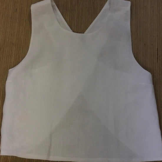 A white sleeveless crop top with a wide scoop neckline, laid flat on a brown woven mat background.