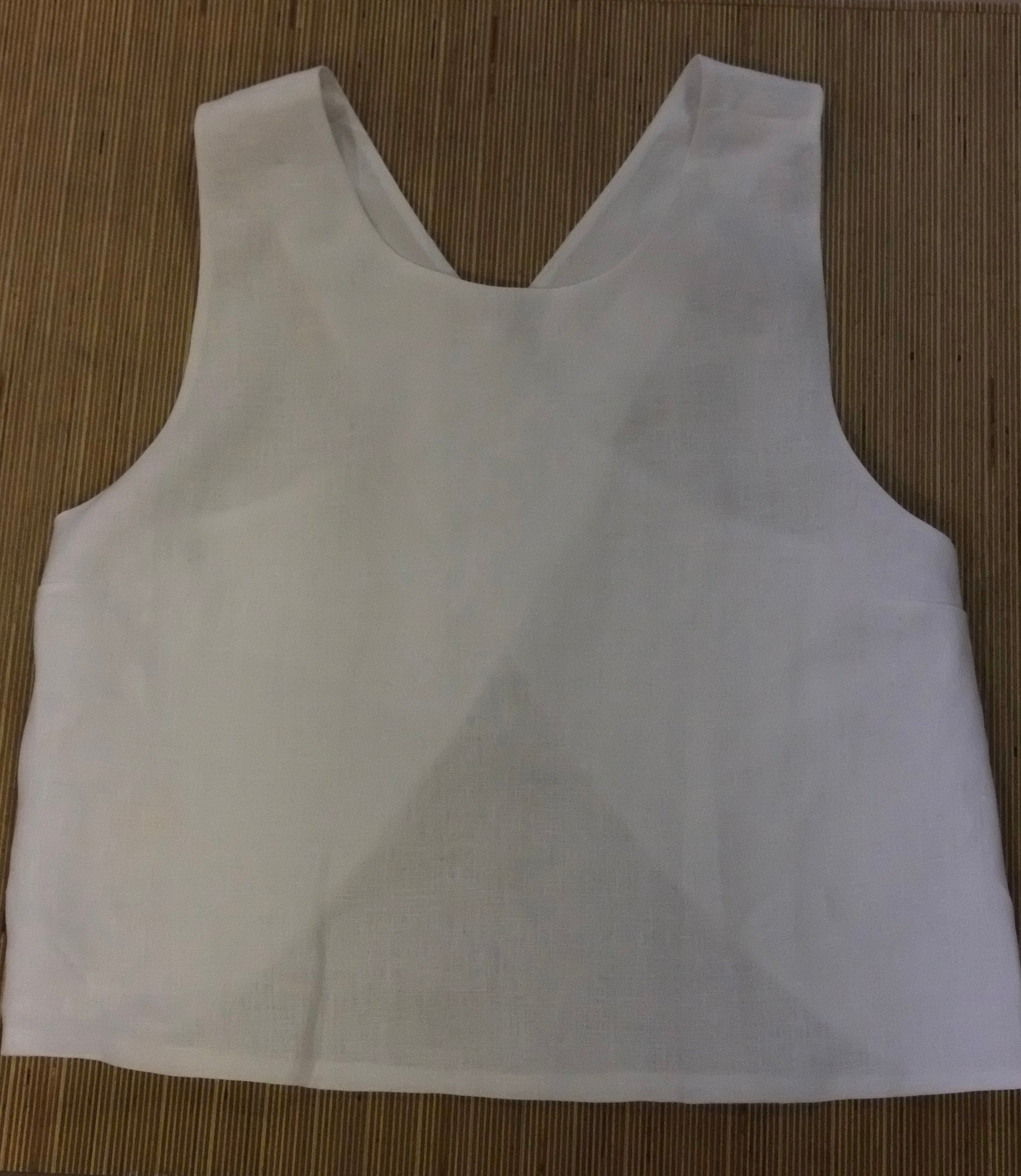 A white sleeveless crop top with a wide scoop neckline, laid flat on a brown woven mat background.