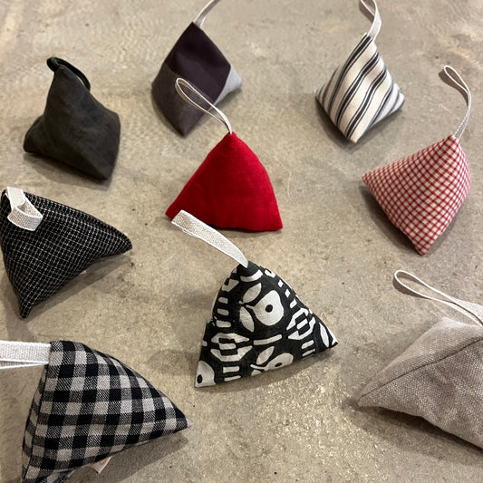 Triangular lavender fabric pouches in various patterns and colours with loop hangers on a concrete surface