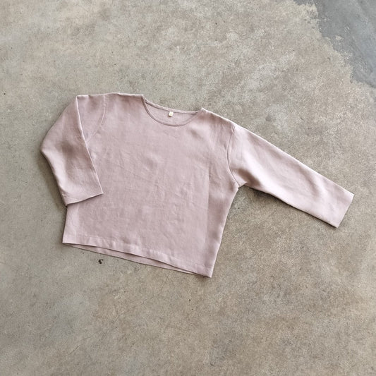 A pink, long-sleeved crop top laid flat on a concrete surface.