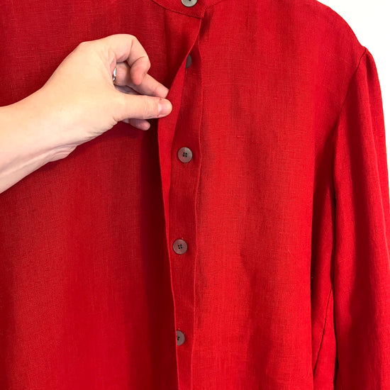 Red shirt with buttons being adjusted by a hand on a white background