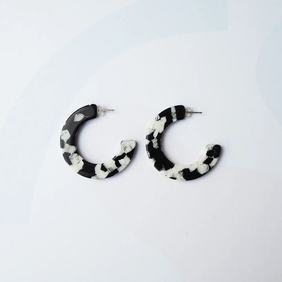 A pair of semi-circular hoop earrings with a black and white marbled pattern, displayed on a clean white background.