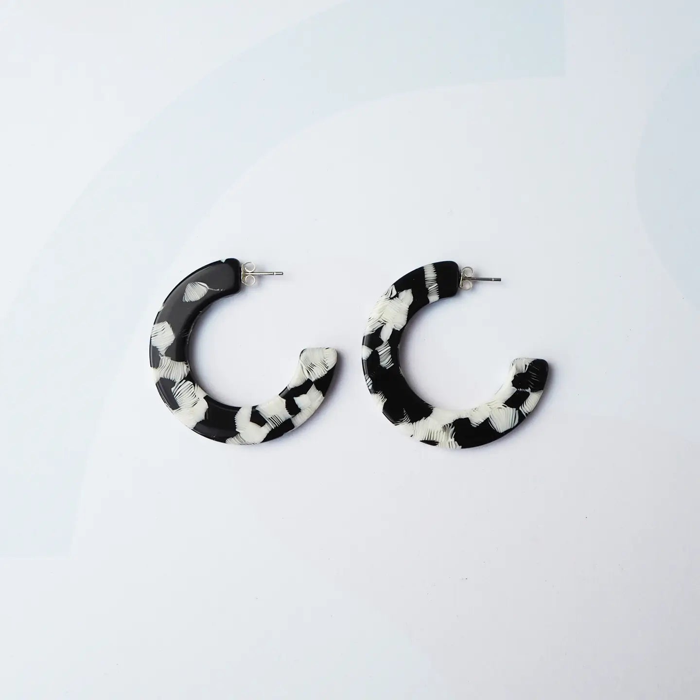 A pair of semi-circular hoop earrings with a black and white marbled pattern, displayed on a clean white background.