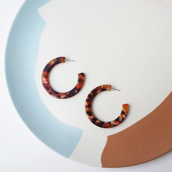 Tortoiseshell hoop earrings on a colorful circular background