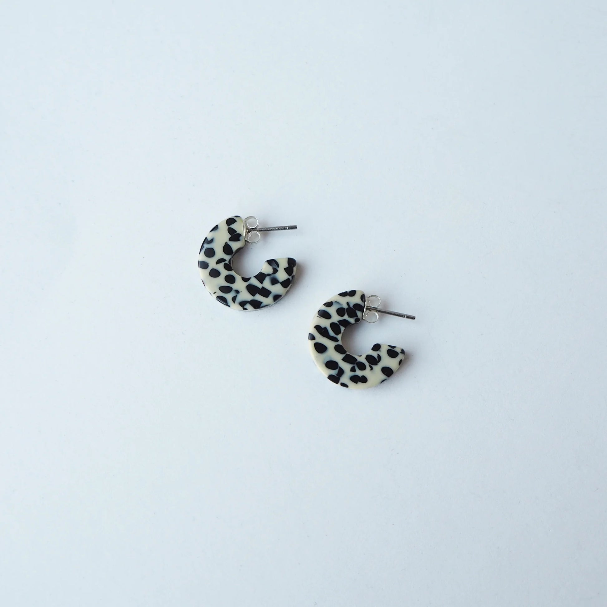 Pair of terrazzo cream and black hoop earrings on a light grey background