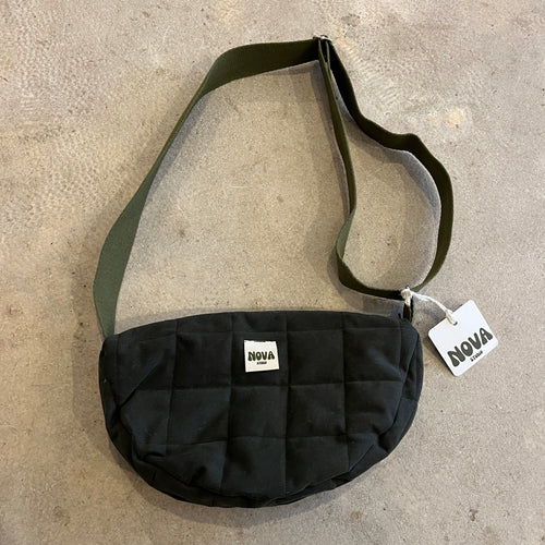 Forest green cotton padded cross body bag with adjustable strap and zip on grey concrete background