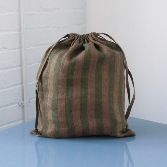 Striped drawstring bag on a reflective surface with a white brick wall background