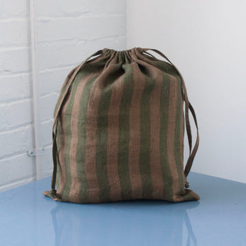 Striped drawstring bag on a reflective surface with a white brick wall background
