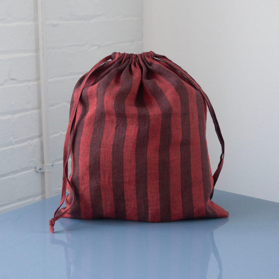 Red and brown striped drawstring bag on a light blue surface with a white brick wall background