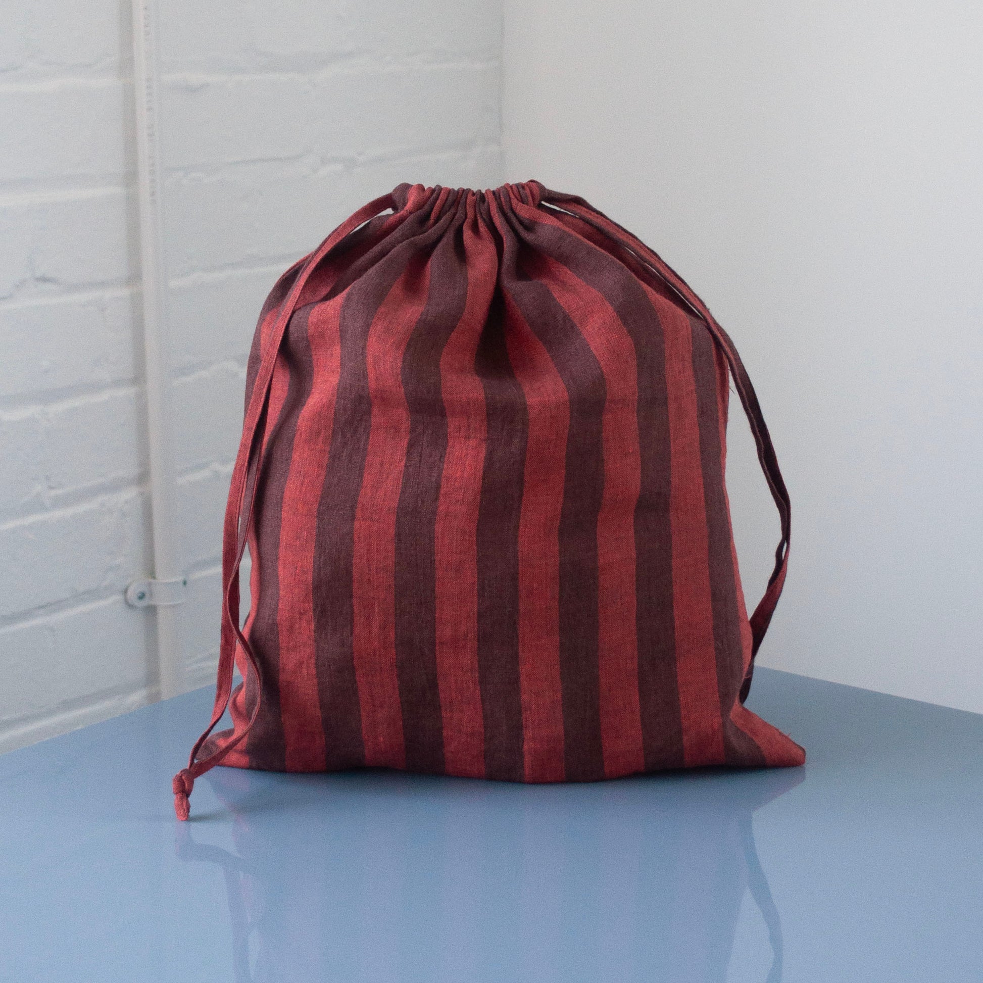 Red and brown striped drawstring bag on a light blue surface with a white brick wall background