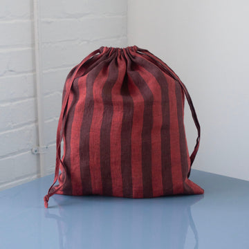 Red and brown striped drawstring bag on a light blue surface with a white brick wall background