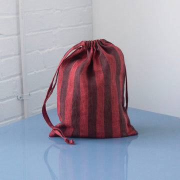 Red and brown striped drawstring bag on a light blue surface with a white brick wall background