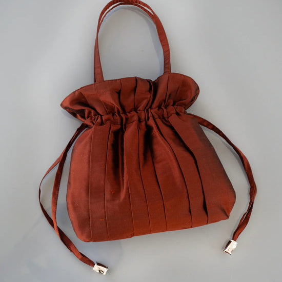 Brown drawstring silk bag with a top handle and side toggles on a grey background