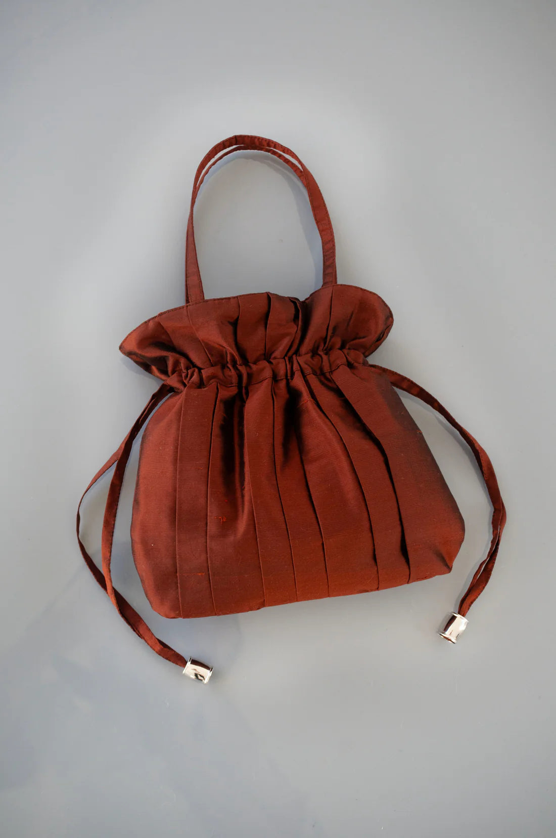 Brown drawstring silk bag with a top handle and side toggles on a grey background