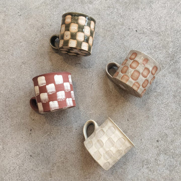 Four ceramic mugs with checkered patterns on a gray surface