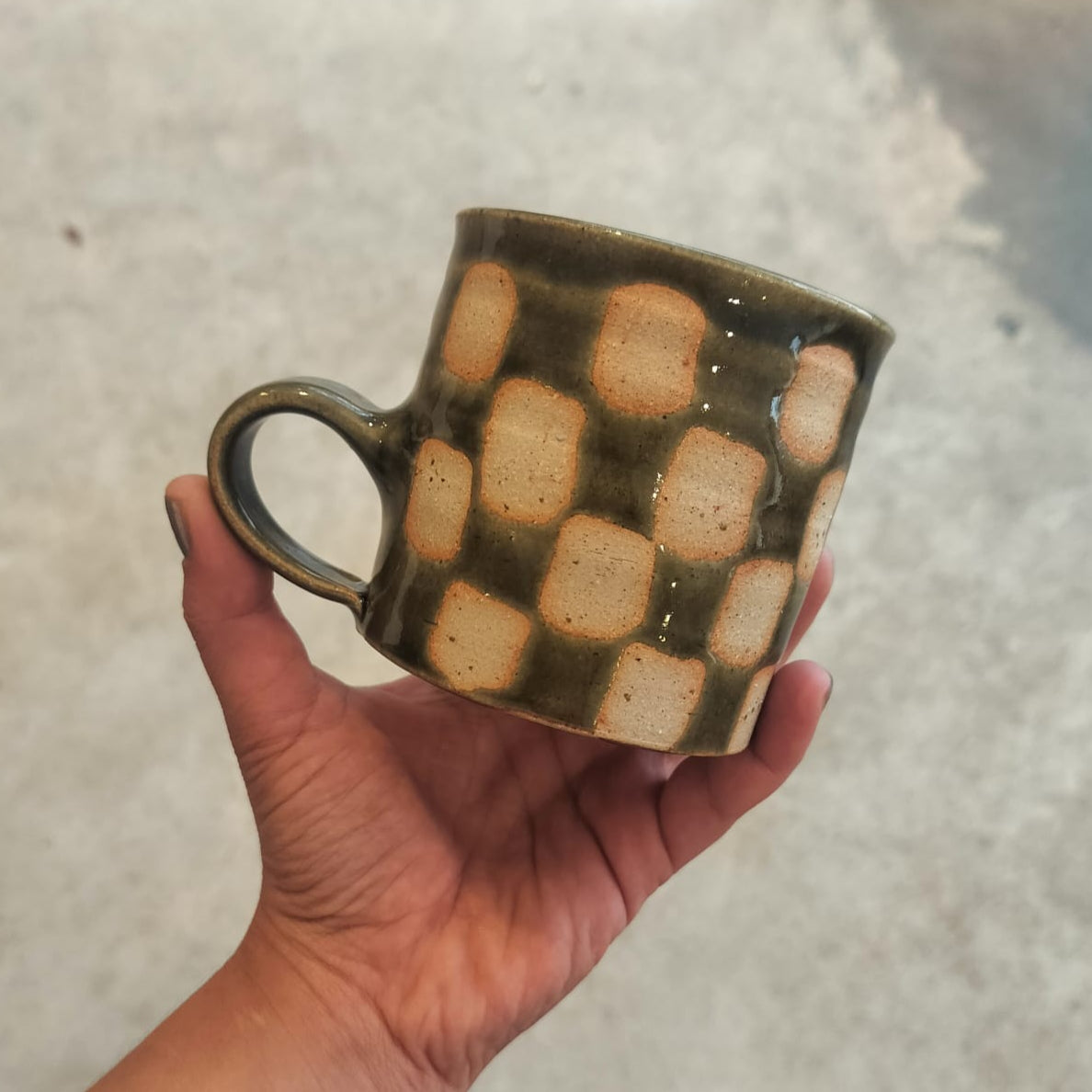 Hand holding a ceramic mug with checkered pattern against a neutral background