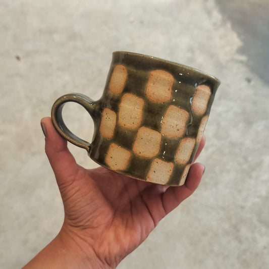 Hand holding a ceramic mug with checkered pattern against a neutral background