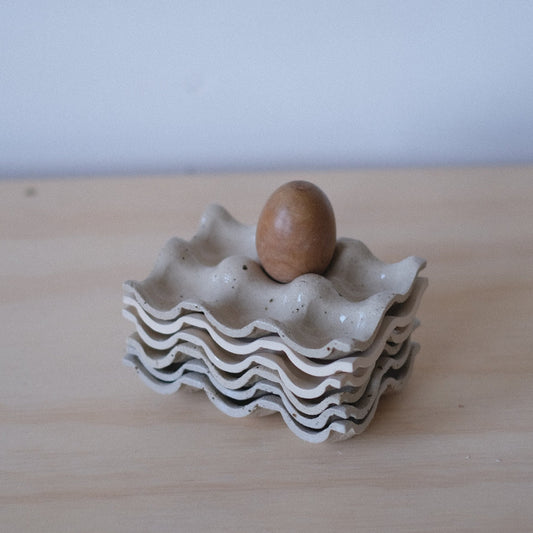 Small white ceramic egg holder with a single brown egg on a light wooden surface.