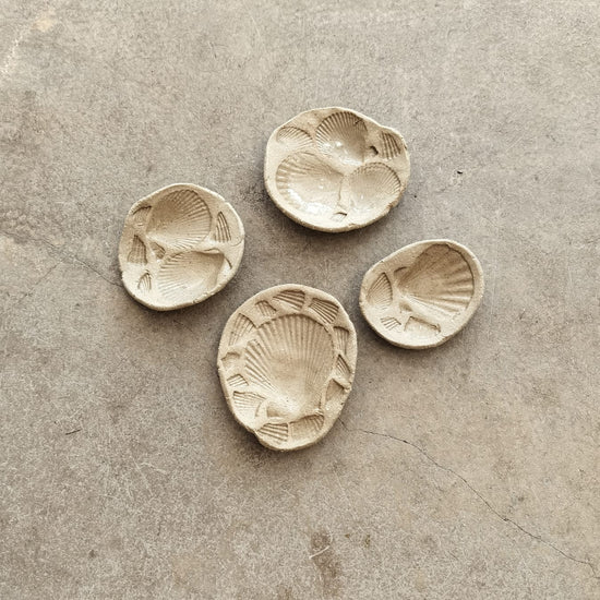 Four ceramic shell-shaped dishes on a textured surface