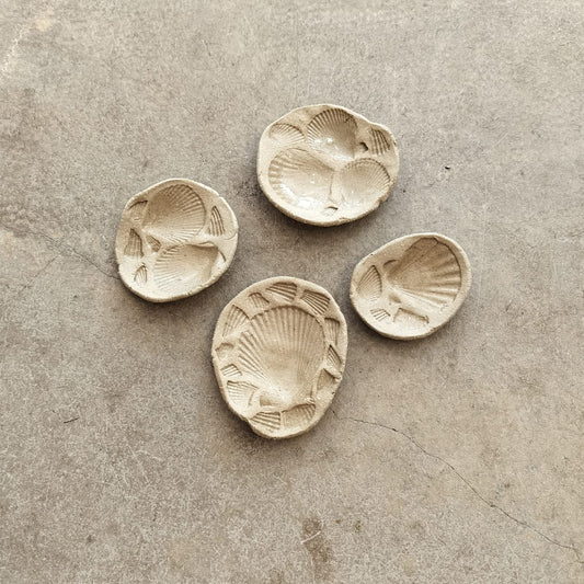 Four ceramic shell-shaped dishes on a textured surface