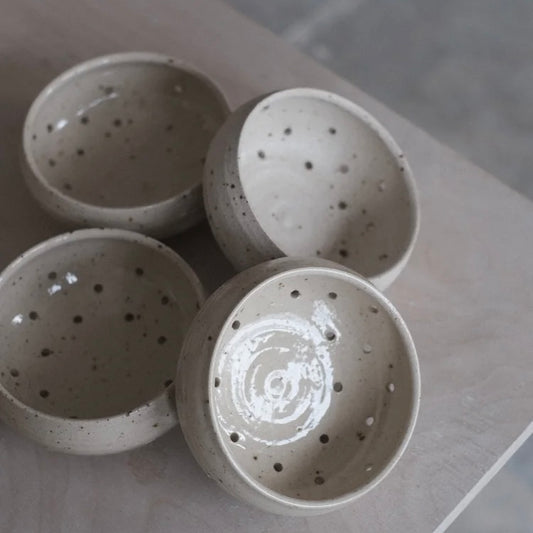 Four grey speckled berry bowls with water drainage holes stacked sitting on a table edge on a grey background