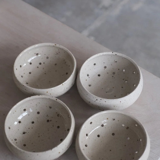 Four grey speckled berry bowls with water drainage holes sitting on a table edge on a grey background