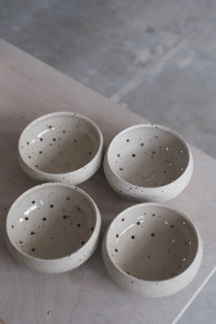Four grey speckled berry bowls with water drainage holes sitting on a table edge on a grey background