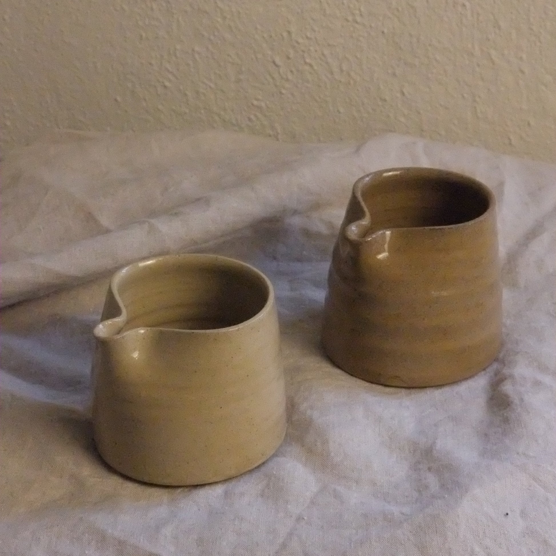 Two ceramic cups on a textured white surface with a beige wall background