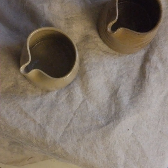 Two ceramic pitchers on a textured surface