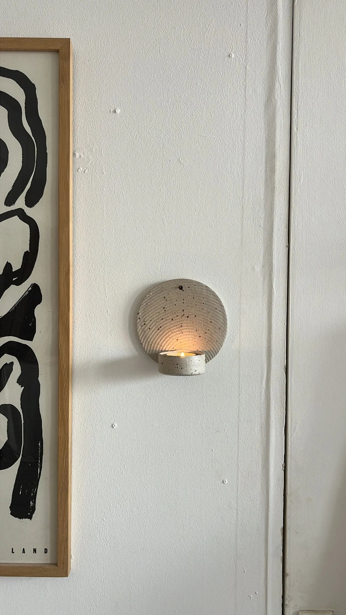 Framed abstract art on a wall with a round wall sconce below.