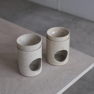 Two ceramic containers with circular holes on a wooden surface.