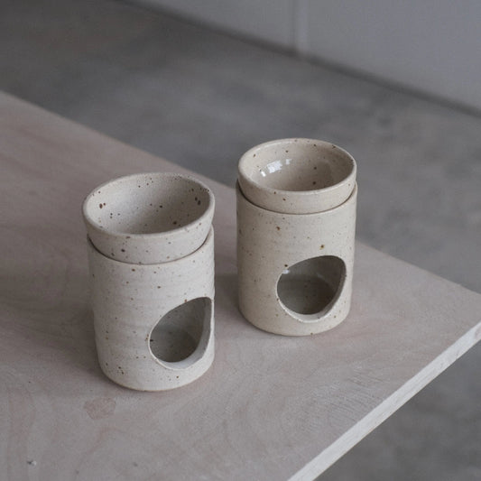 Two ceramic containers with circular holes on a wooden surface.