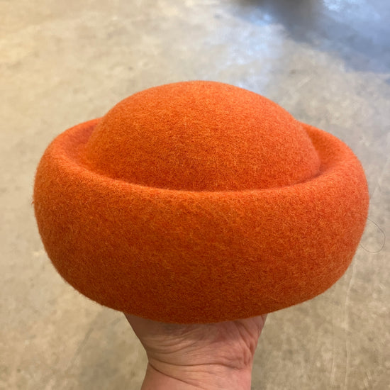 Orange felted product held by a hand on a neutral background