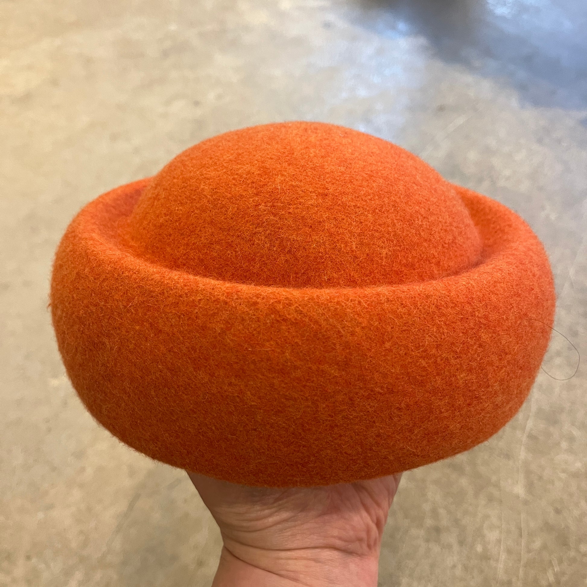 Orange felted product held by a hand on a neutral background