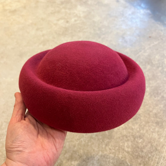 Red felt hat held by a hand on a light-colored surface