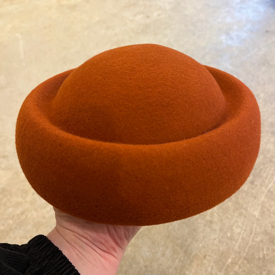 Brown felt hat held by a person against a neutral background