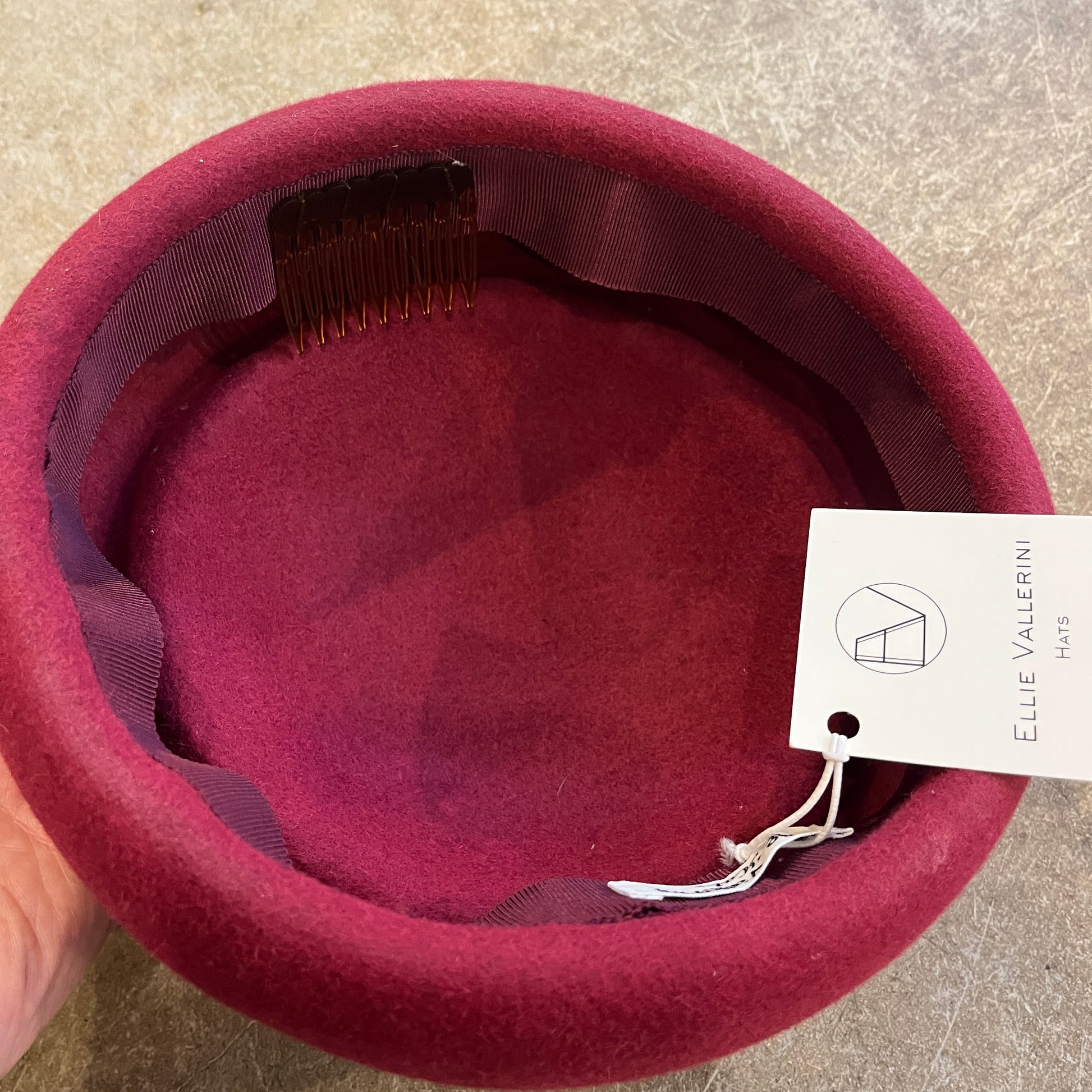 Maroon hat with a visible brand tag on a beige surface