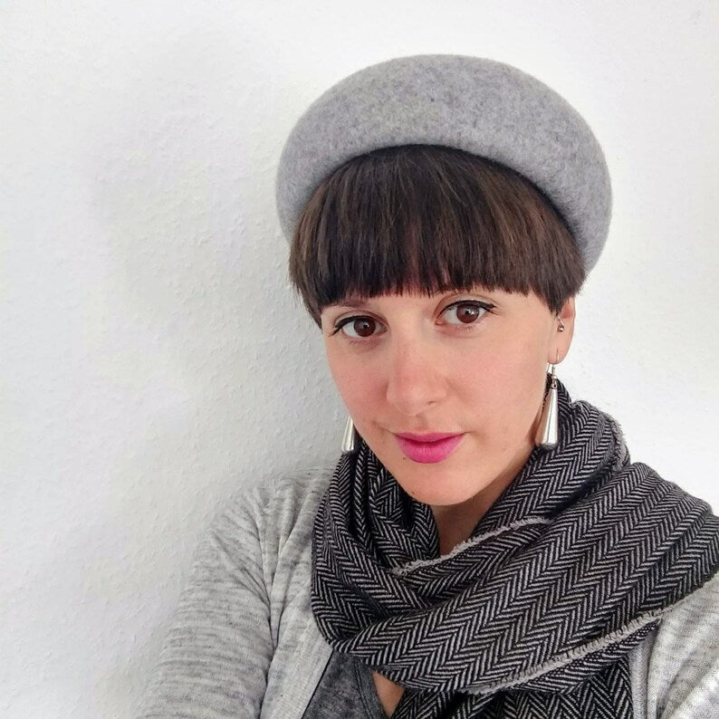 Woman wearing a gray beret and scarf against a white background