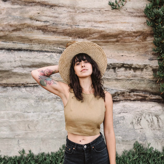 Woman wearing a straw hat and beige top against a stone wall