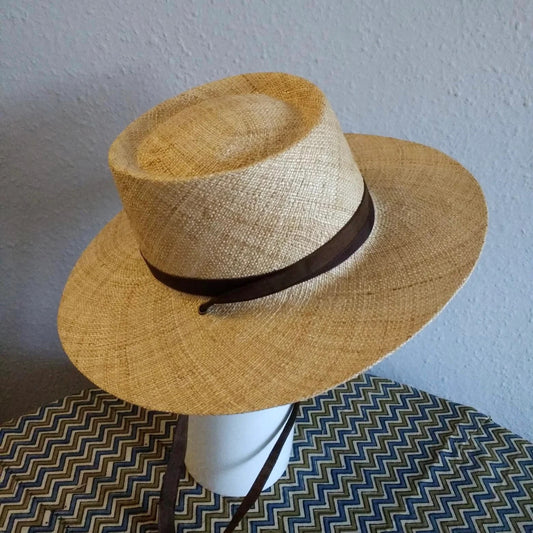 Beige straw hat with a brown band on a mannequin head against a light blue wall.