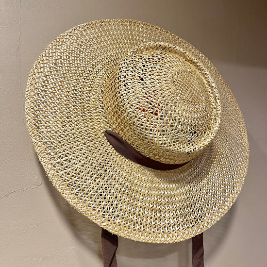 Woven straw hat on a stand against a neutral background