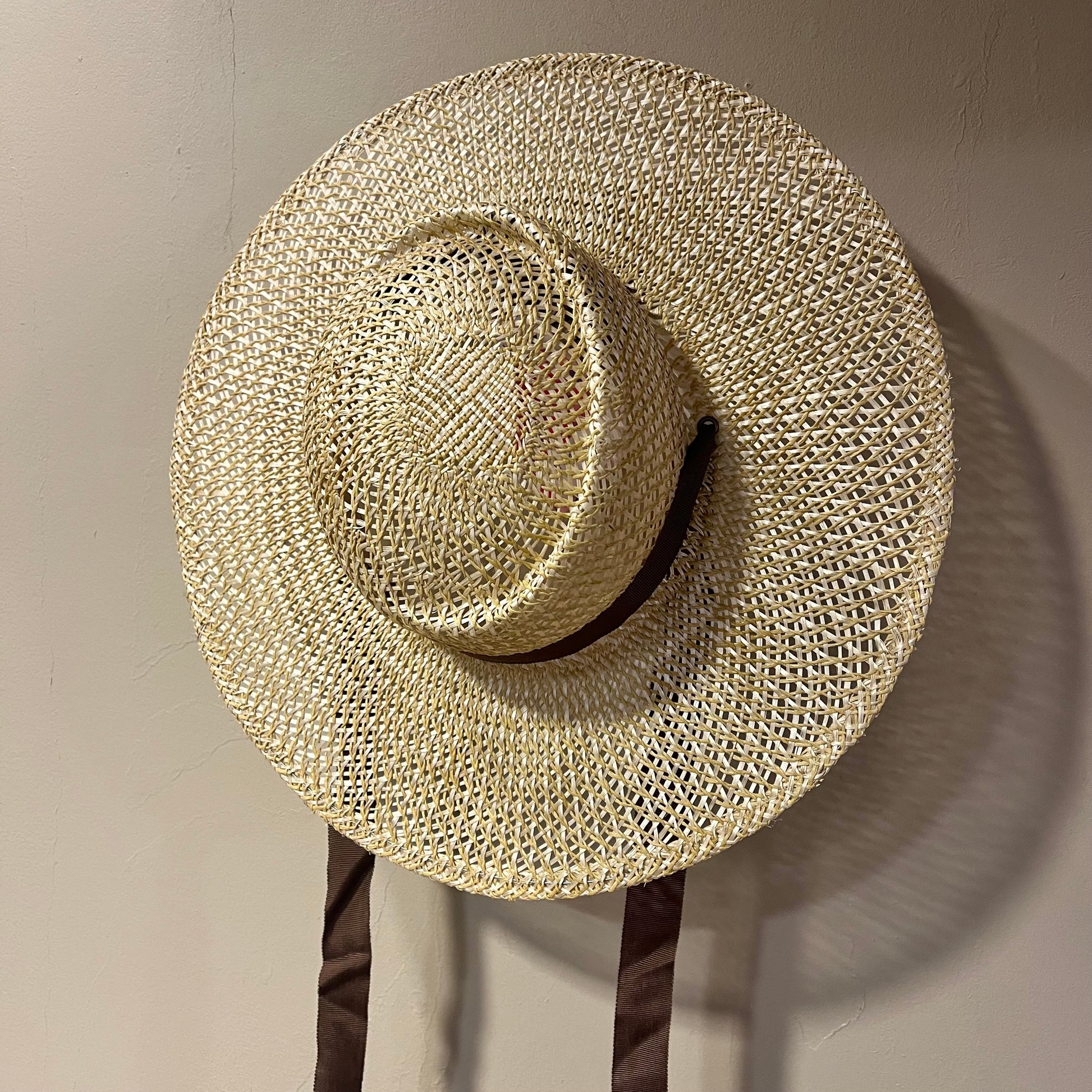 Beige straw hat on a stand against a plain wall